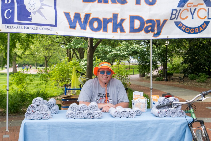 John Fiori sitting behind a table containing stacks of rolled t-shirts