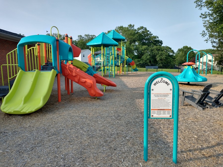 A closer view of the playground at the Community Park at Church Road, with a Welcome sign in the foreground.